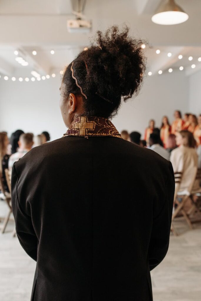 A pastor stands at the altar in a modern church setup with parishioners and a choir in the background.